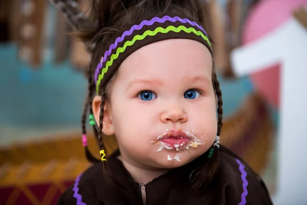 Küçük şirin kız Apache Hint Baş kostüm ve tüy headdress oturur ve tatlı bir kek tadı. İlk doğum günü pastası 1 yıl ve smash — Stok fotoğraf