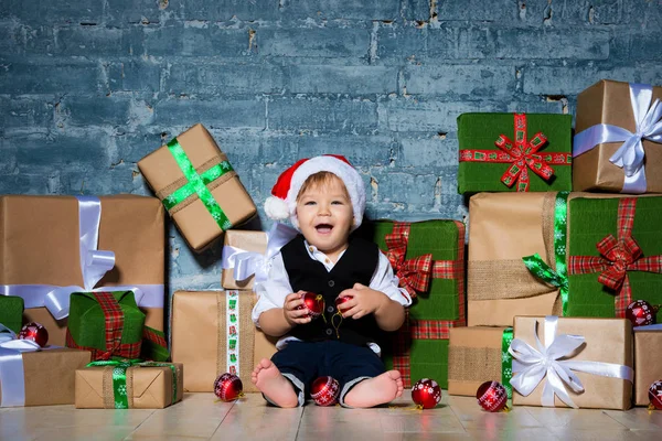 Pequeño bebé sonriente Santa Claus en sombrero de Navidad y traje de negocios. Feliz año nuevo y feliz Navidad. Vacaciones y regalos para niños —  Fotos de Stock