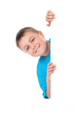 Parlak mavi t-shirt ve izole beyaz arka plan üzerinde beyaz bir panelin arkasında poz gülümseyen duygusal olumlu genç çocuk. Reklam için yer