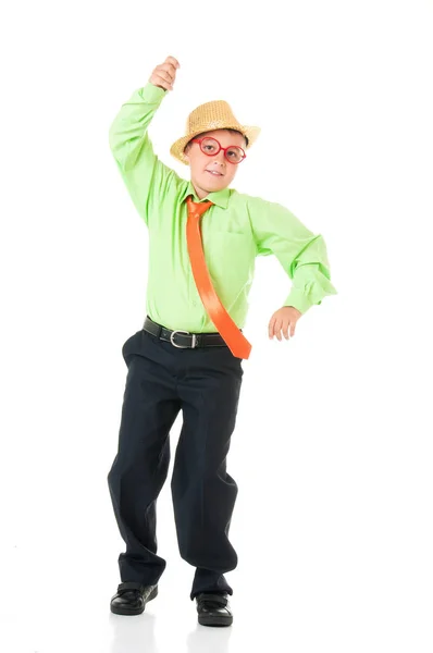 Divertente ragazzo scolaro in un abito da lavoro, cravatta luminosa e occhiali divertenti e un cappello emotivamente ballare su uno sfondo bianco isolato — Foto Stock