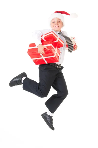 Мальчик в белой рубашке и шляпе новогоднего Санта-Клауса прыгает с красными подарками. Изолированный белый фон — стоковое фото