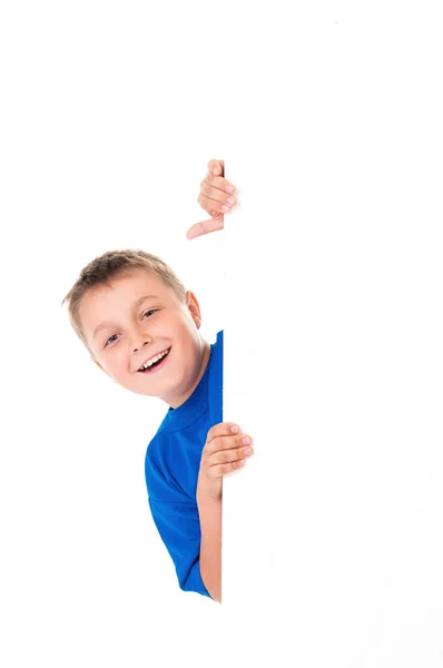 Un adolescente guapo sonriente vestido con una camiseta azul brillante y posando detrás de un panel blanco aislado sobre fondo blanco. Lugar para la publicidad — Foto de Stock