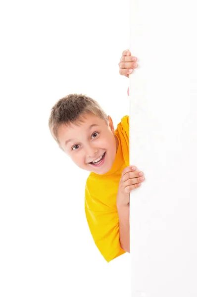 A smiling handsome teenager boy wearing a bright yellow t-shirt and posing behind a white panel isolated on white background. Place for advertising Stock Picture