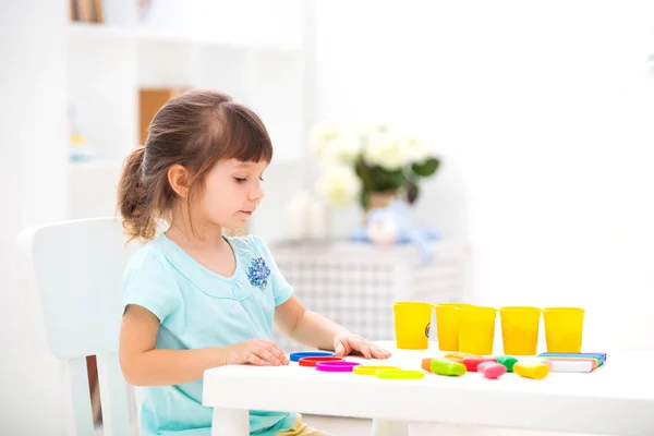 Piccola bella ragazza scolpisce da plastilina al tavolo al suo interno. Sviluppo del bambino e capacità motorie. Creatività dei bambini — Foto Stock