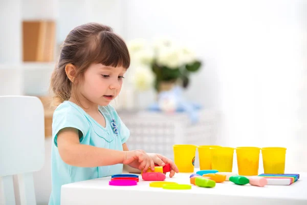 Little beautiful girl sculpts from plasticine at the table in the interior. Child development and fine motor skills. Children's creativity — Stock Photo, Image