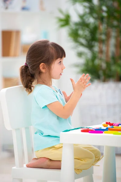 Маленькая красивая девочка скульптуры из пластилина за столом в интерьере. Развитие ребенка и мелкая моторика. Детское творчество — стоковое фото