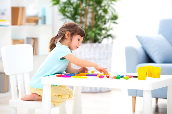 Una bonita niña de tres años se sienta a la mesa y esculpe figuras de arcilla de colores. Escultura y creatividad infantil —  Fotos de Stock