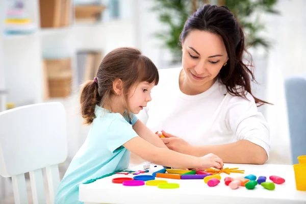 La madre sonriente ayuda a una pequeña hija a esculpir figuras de plastilina. Creatividad infantil. Familia feliz — Foto de Stock