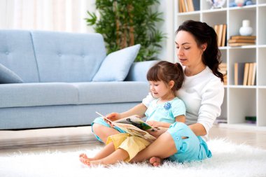 Güzel genç Anne kızı odada katta halı oturan bir kitap okuma. Çocuklarla okuma