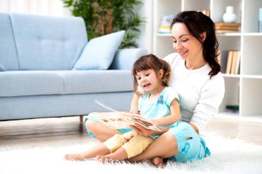 Güzel genç Anne kızı odada katta halı oturan bir kitap okuma. Çocuklarla okuma