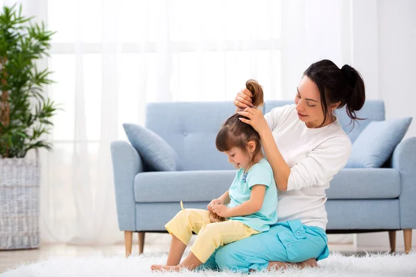 Щаслива любляча сім'я. Мама розчісує волосся своєї дочки, сидячи на килимі на підлозі в кімнаті — стокове фото