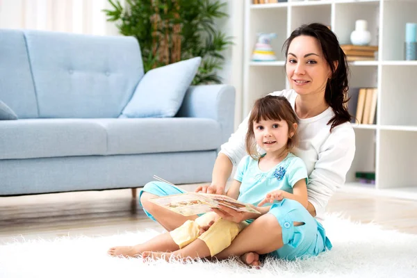 Feliz familia amorosa. Hermosa madre e hija pequeña se divierten, juegan en la habitación en el suelo, abrazan, sonríen y tontean —  Fotos de Stock