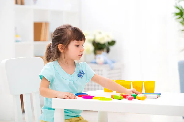 Kreatywność dzieci. Dzieciak rzeźbi z gliny. Cute little formy dziewczyna z plasteliny na stole w pokoju — Zdjęcie stockowe