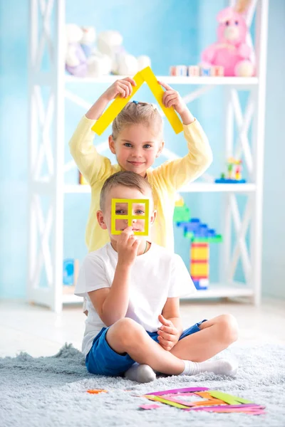 Una bambina con un ragazzo è seduta sul pavimento e tiene in mano una casa di carta colorata . — Foto Stock