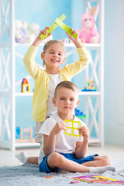 Küçük bir kız bir çocukla katta oturan ve renkli kağıttan bir ev tutarak.