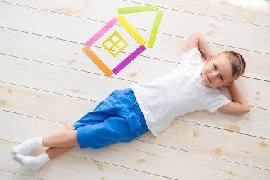 küçük çocuk renkli kağıttan bir evin yanındaki yerde yatıyor