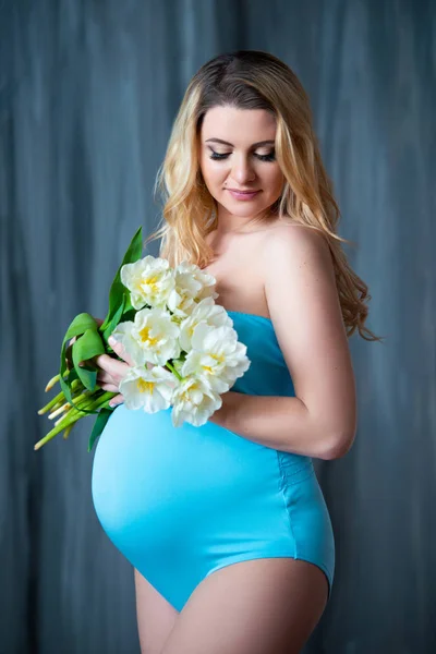Beautiful young pregnant blonde woman holding flowers white tulips in her hands. Spring mood, freshness, women\'s Day, health and beautiful pregnancy