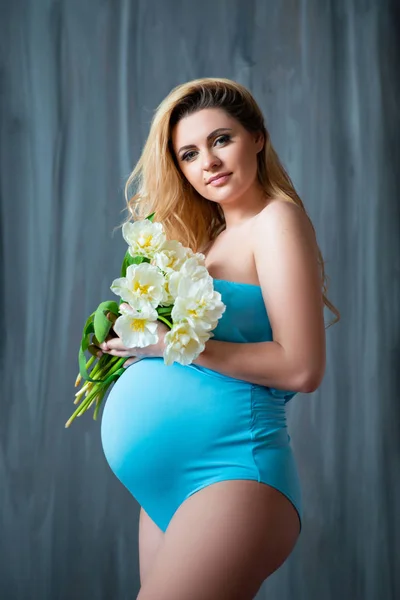 Schöne junge schwangere blonde Frau mit Blumen weiße Tulpen in ihren Händen. Frühlingsstimmung, Frische, Frauentag, Gesundheit und schöne Schwangerschaft — Stockfoto