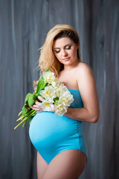 Красивая молодая беременная блондинка с цветами белых тюльпанов в руках. Весеннее настроение, свежесть, женский день, здоровье и красивая беременность — стоковое фото