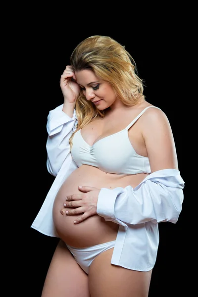 Όμορφη χαμογελαστή ξανθιά έγκυος γυναίκα με λευκά ρούχα σε μαύρο φόντο. Υγεία των γυναικών και ευτυχισμένη εγκυμοσύνη — Φωτογραφία Αρχείου