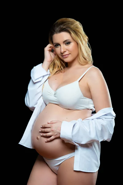 Frumoasă blondă gravidă în haine albe pe un fundal negru. Sănătatea femeilor și sarcina fericită — Fotografie, imagine de stoc