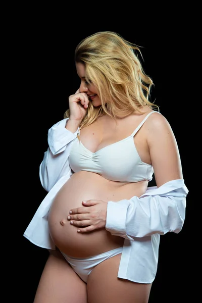 Frumos zâmbind blondă femeie gravidă în haine albe pe un fundal negru. Sănătatea femeilor și sarcina fericită — Fotografie, imagine de stoc