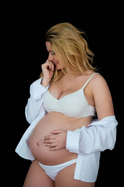 Mooie lachende blonde zwangere vrouw in witte kleren op een zwarte achtergrond. Vrouwen gezondheid en gelukkige zwangerschap — Stockfoto