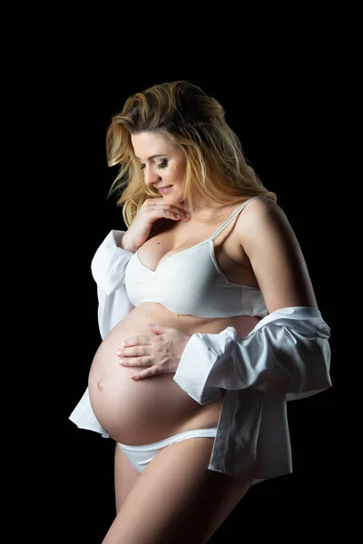 Gyönyörű szőke terhes nő, fehér ruhát egy fekete háttér. A nők egészsége és boldog terhesség — Stock Fotó