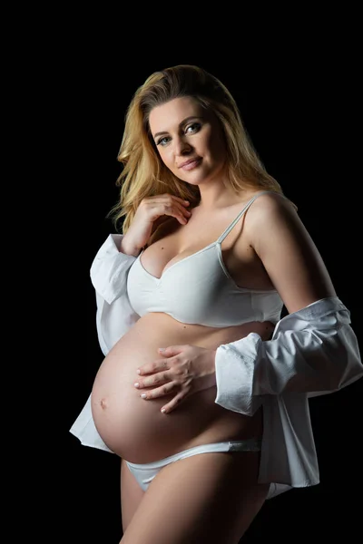 Mooie blonde zwangere vrouw in witte kleren op een zwarte achtergrond. Vrouwen gezondheid en gelukkige zwangerschap — Stockfoto