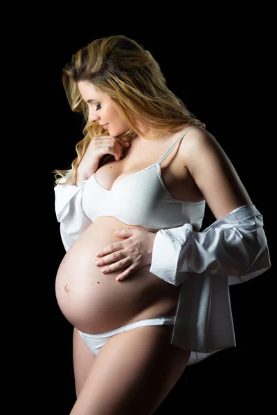 Schöne blonde schwangere Frau in weißer Kleidung auf schwarzem Hintergrund. Gesundheit der Frauen und glückliche Schwangerschaft — Stockfoto