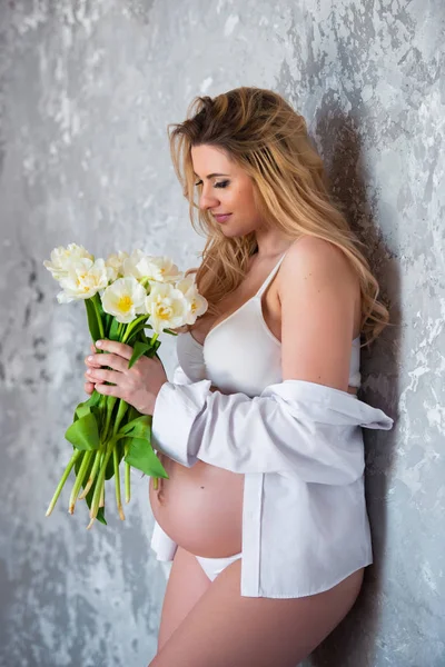 Krásná mladá těhotná blondýnka miluje květiny bílé tulipány. Jarní nálada, čerstvost, den žen, zdraví a krásné těhotenství — Stock fotografie