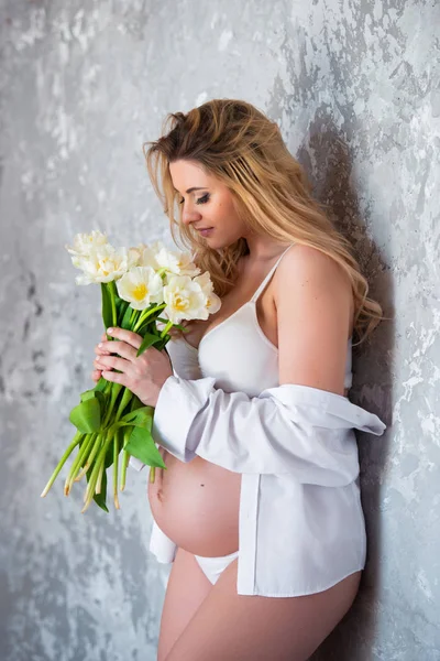 Beautiful young pregnant blonde woman love flowers white tulips. Spring mood, freshness, women\'s Day, health and beautiful pregnancy