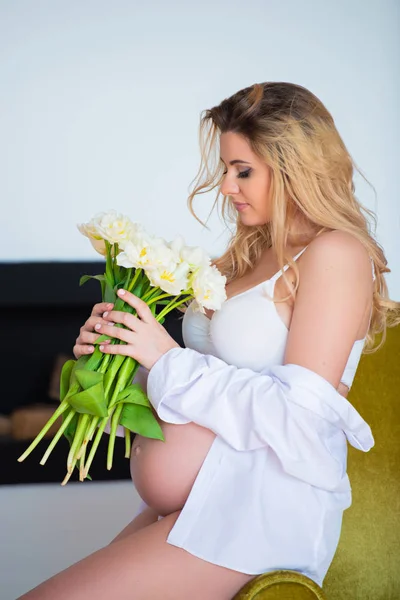 Frumoasă femeie însărcinată cu flori albe de primăvară în mână în interior. Cadou feminin, concept de încălzire a casei, sănătate și sarcină fericită — Fotografie, imagine de stoc