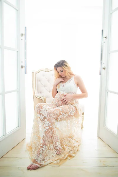 Güzel bir dantel elbise güzel hamile kadın açık kapı yakınında bir vintage sandalyede oturuyor. Yeni bir hayatın başlangıcı ve mutlu bir hamilelik — Stok fotoğraf