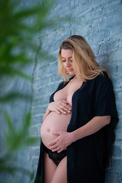 Μια όμορφη έγκυο γυναίκα με μαύρη ρόμπα στέκεται πάνω στον γκρίζο τοίχο του τούβλου. Θηλυκή σεξουαλικότητα, θηλυκότητα και όμορφη εγκυμοσύνη — Φωτογραφία Αρχείου