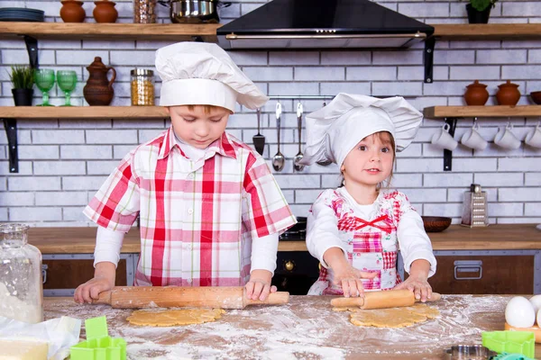 Children brother and sister bake gingerbread in the kitchen. A girl and a boy roll out the dough with a rolling pin on the table — Stock Photo, Image