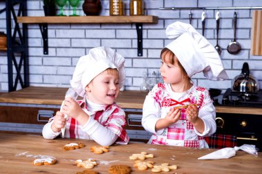 Children a girl and a boy in a cooking chef's hat decorate ready-made baked gingerbread with sweet icing and cream clipart