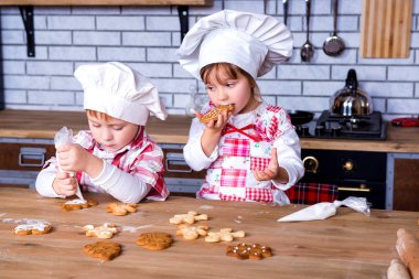 Children a girl and a boy in a cooking chef's hat decorate ready-made baked gingerbread with sweet icing and cream clipart