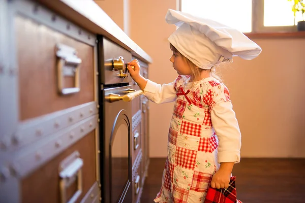 Girl in chef\'s hat is putting gingerbread cookies in the oven