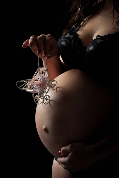 Close-up van vrouw zwangere buik met een speelgoed kinderwagen. Meisje teder houdt haar buik met kind. Concept van zwangerschap, moederdag liefde en gelukkig moederschap — Stockfoto