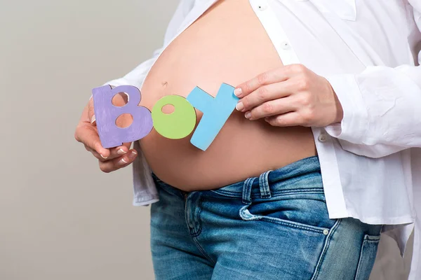 Close-up. Mulher segurando um sinal a palavra menino no fundo de uma barriga grávida — Fotografia de Stock