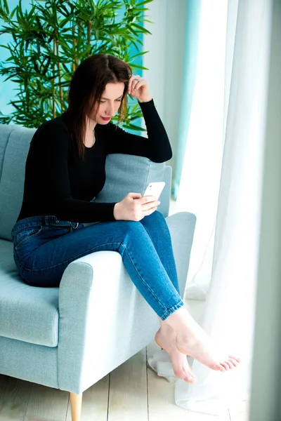 Young happy woman sitting on the sofa at home while talking on phone — Stock Photo, Image