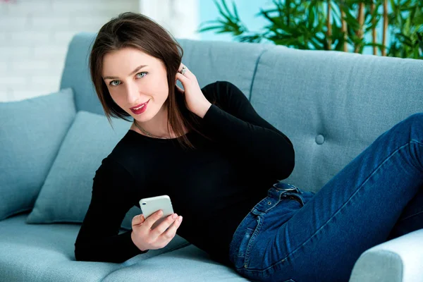 Young happy woman sitting on the sofa at home while talking on phone — Stock Photo, Image