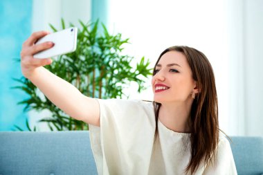 Genç esmer kız kanepede selfie çekiyor.