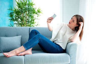 Genç esmer kız kanepede selfie çekiyor..