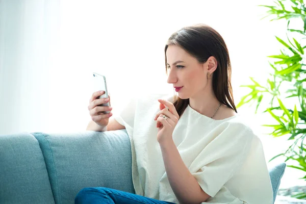 Young woman sitting on a sofa while playing with her smartphone — Stock Photo, Image