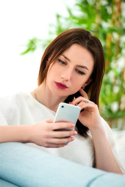 Young woman sitting on a sofa while playing with her smartphone — Stock Photo, Image