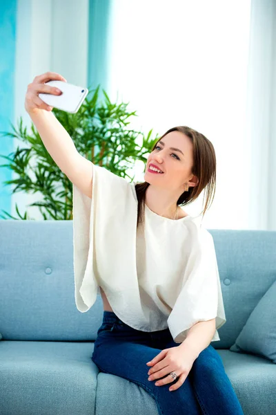 Young brunette girl is making selfie at sofa — Stock Photo, Image