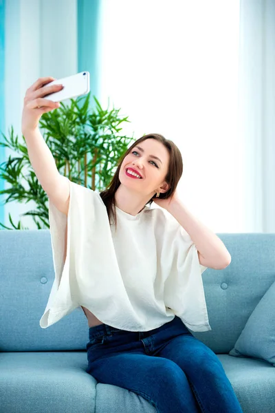 Young brunette girl is making selfie at sofa — Stock Photo, Image