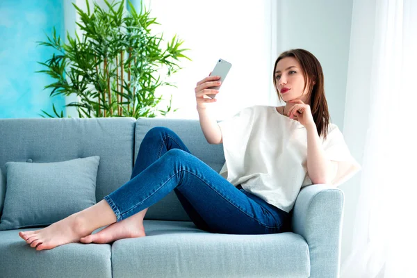 Young brunette girl is making selfie at sofa. — Stock Photo, Image